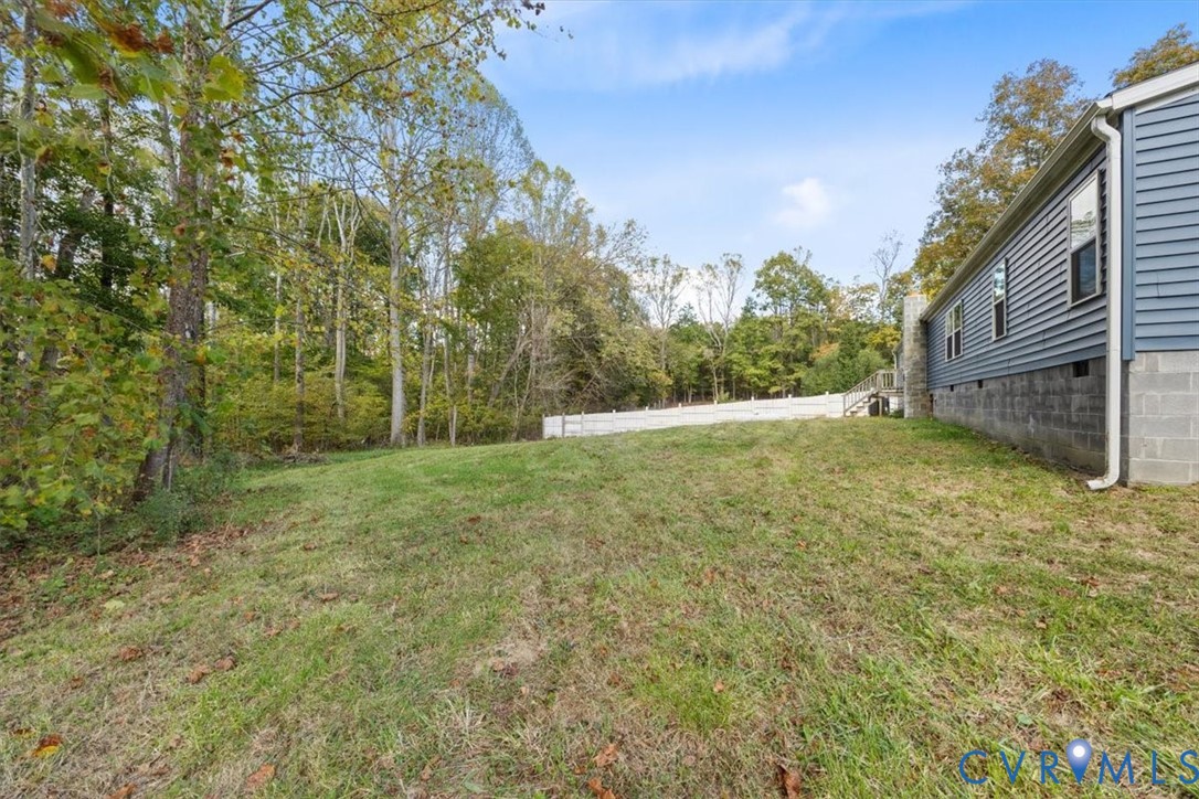 Rear exterior featuring horizontal lap siding, a concrete block foundation, and a white privacy fence bordering a wooded lot