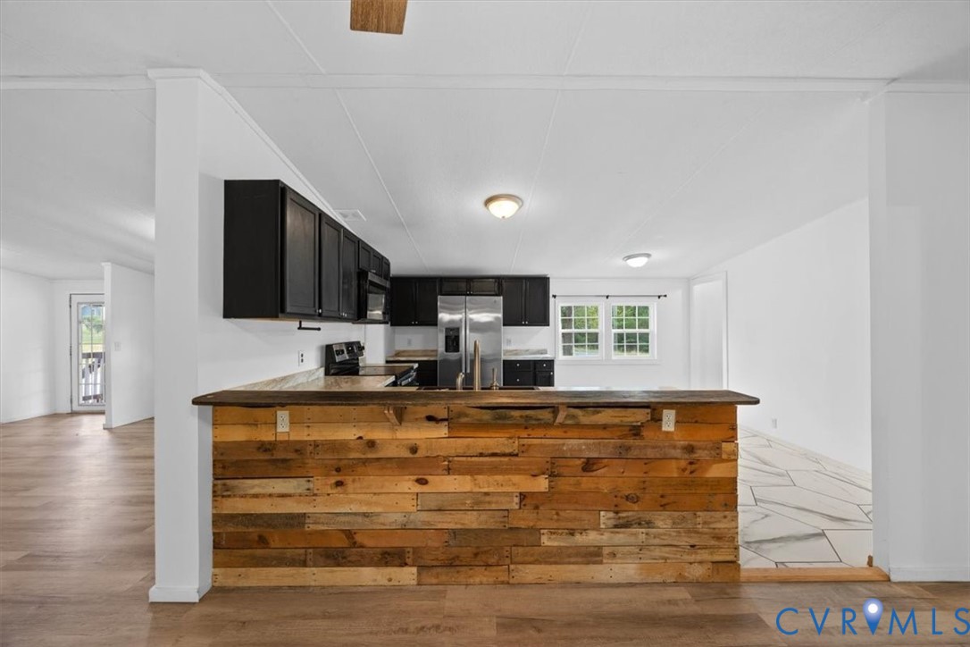 Kitchen featuring a wood-plank breakfast bar, dark-finish cabinetry, stainless steel appliances, and wood-finish flooring