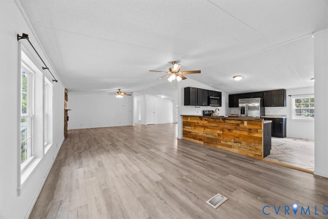 Open-concept interior featuring wood-finish flooring, a kitchen island with reclaimed wood cladding, dark cabinetry, stainless steel appliances, and dual ceiling fans