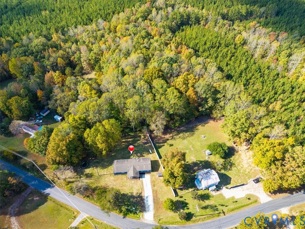Aerial perspective featuring expansive acreage, mature perimeter woodland, paved driveway, and open grass areas