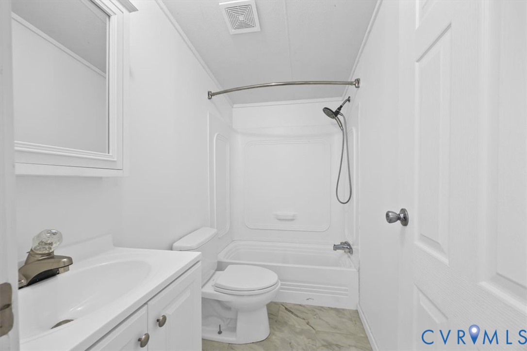 Main Hall Bathroom featuring a vanity cabinet with a integrated sink, a built-in medicine cabinet with mirror, a toilet, a shower and tub combination with a handheld shower head, and patterned flooring