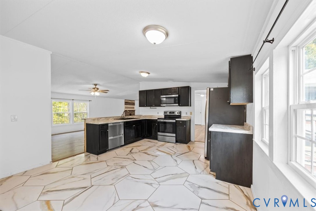Kitchen featuring dark cabinetry, stone-finish countertops, stainless steel appliances, and large-format geometric marble tile flooring