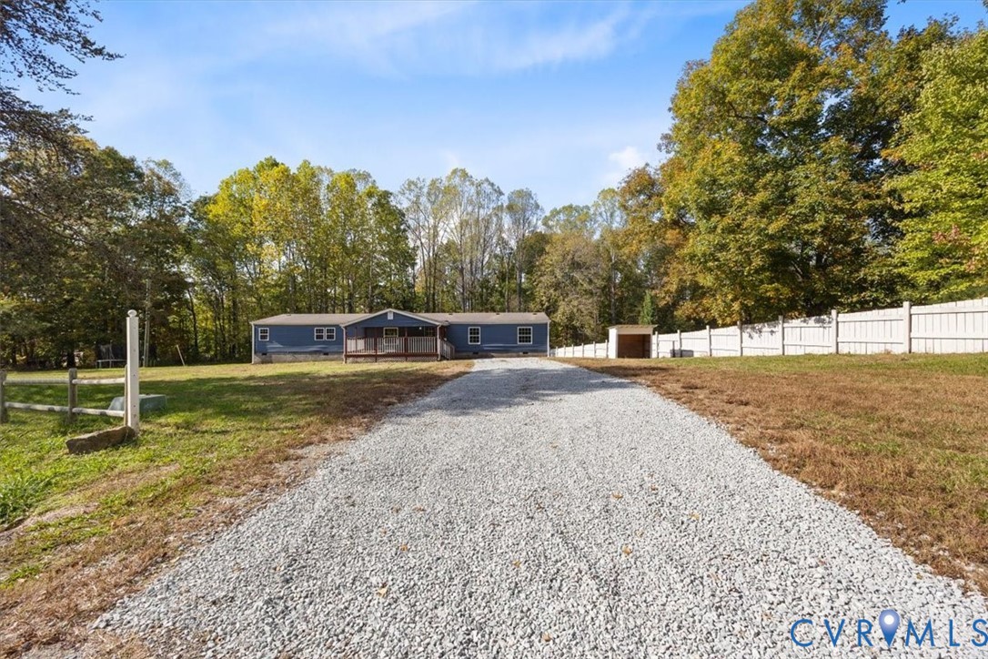 Blue exterior siding, front entry deck, gravel driveway, and perimeter fencing situated on a wooded lot