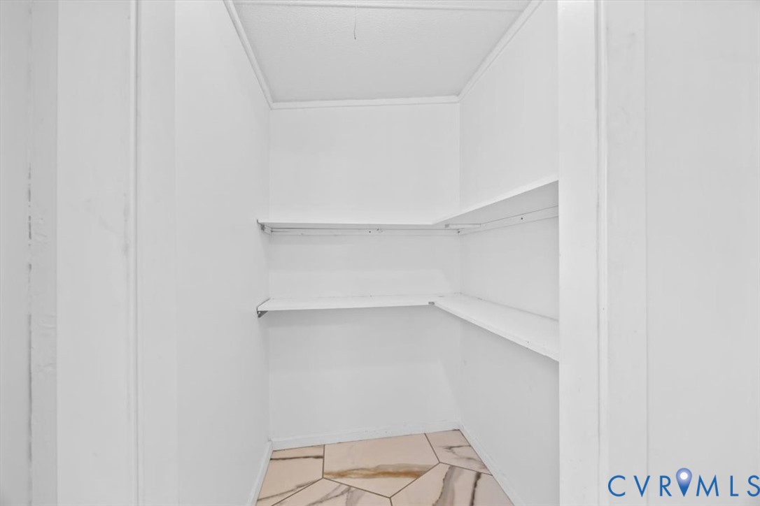 Storage area featuring multi-level white shelving and neutral-toned tile flooring