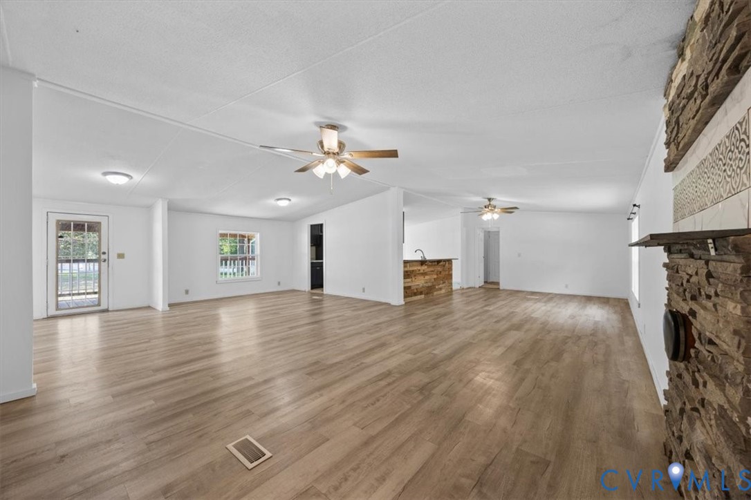 Open-concept interior featuring wood-finish flooring, a textured stone fireplace, dual ceiling fans, and a kitchen island with stone detailing