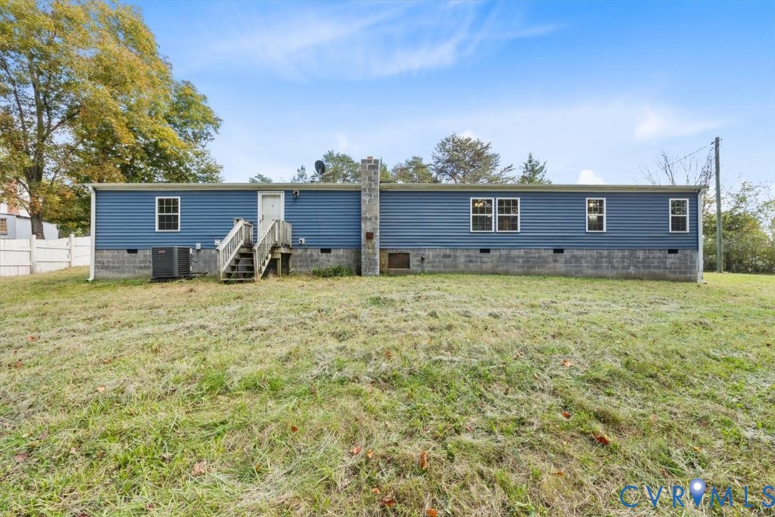 Exterior featuring horizontal siding, a stone-veneer chimney, concrete block foundation, wooden stairs, and a level lawn