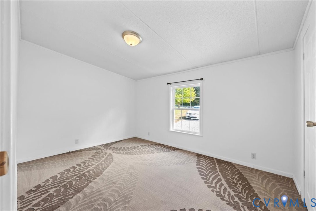 Neutral interior space featuring patterned wall-to-wall carpeting, white walls, a flush-mount ceiling light fixture, and a single-hung window with a dark hardware rod
