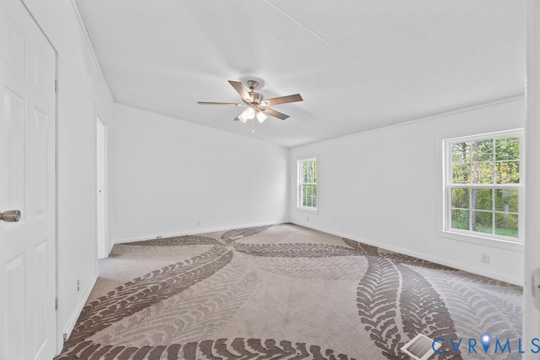 Interior room featuring patterned wall-to-wall carpeting, brushed-nickel ceiling fan with integrated lighting, and multiple windows
