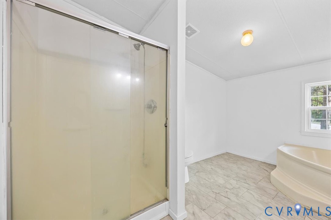 Bathroom featuring a glass-enclosed shower, a soaking tub, stone-finish tile flooring, and a single-pane window