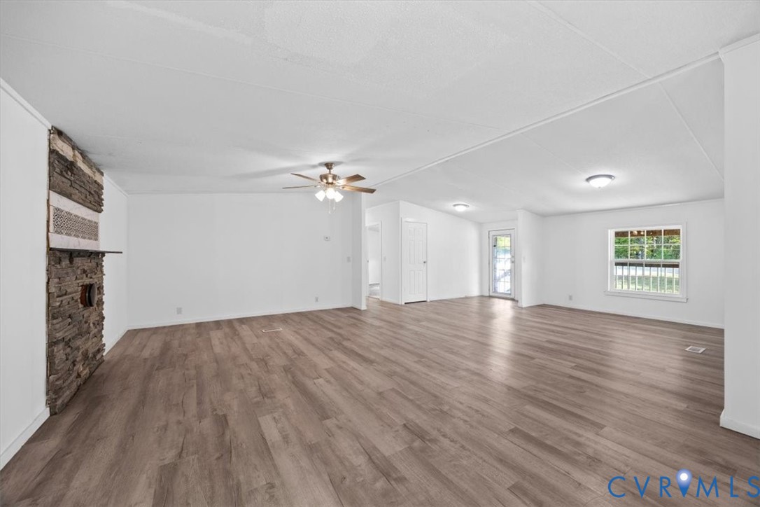 Spacious interior featuring wood-finish flooring, a floor-to-ceiling stone-accented hearth, ceiling fan, and large windows