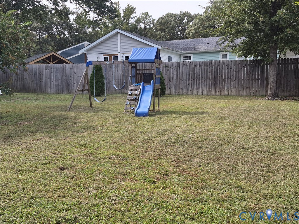 Expansive grassed yard featuring a wooden privacy fence and mature trees
