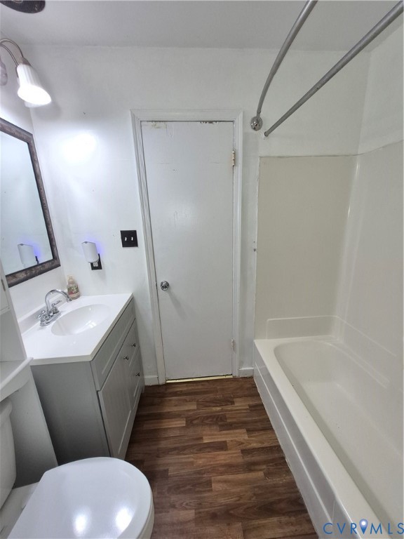Bathroom featuring a full-sized tub with shower, single vanity with integrated sink, wood-finish flooring, and wall-mounted light fixture