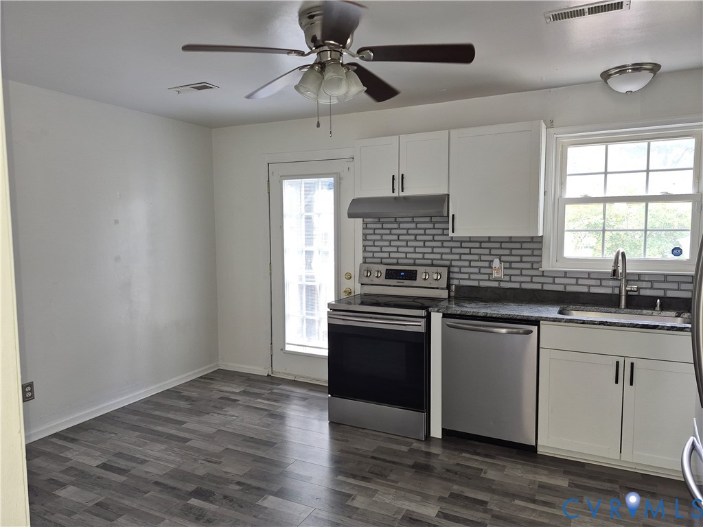 Kitchen featuring wood-finish flooring, white cabinetry, dark countertops, a subway tile backsplash, and stainless steel appliances