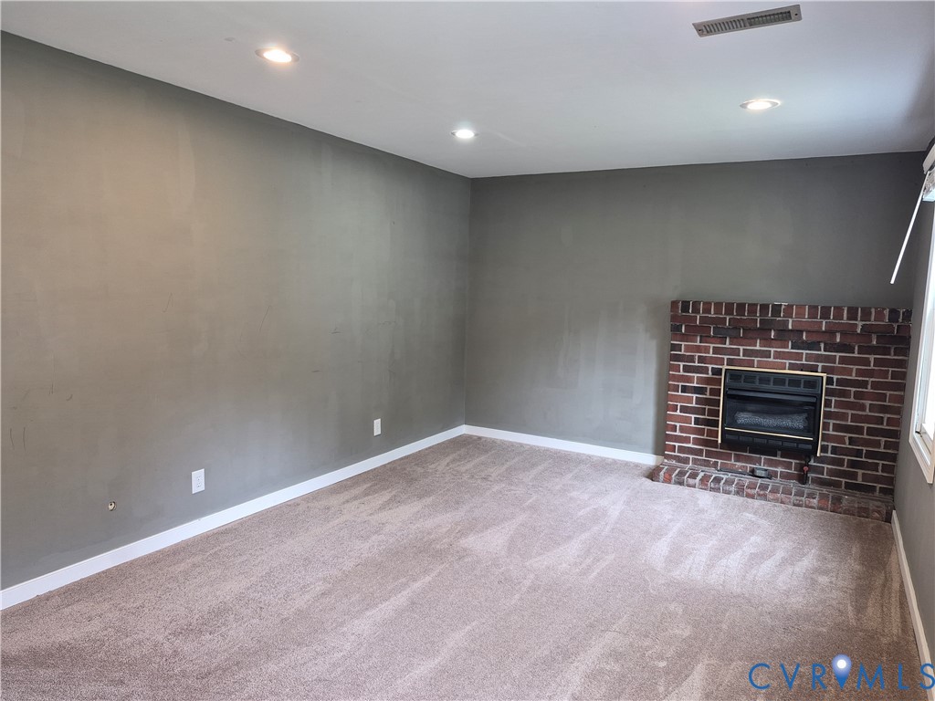 Recessed lighting, brick fireplace with gas insert, light-toned carpet, and neutral wall paint
