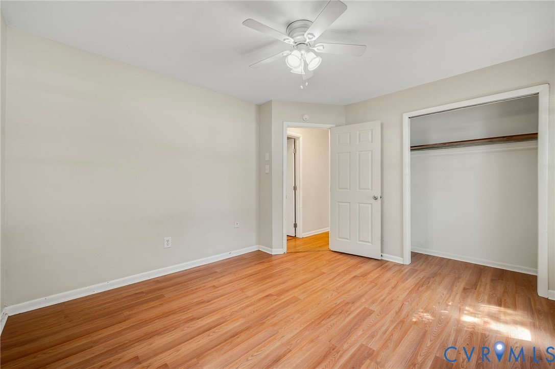 Wood-finish flooring throughout, white ceiling fan with light fixture, and an open closet with a clothes rod