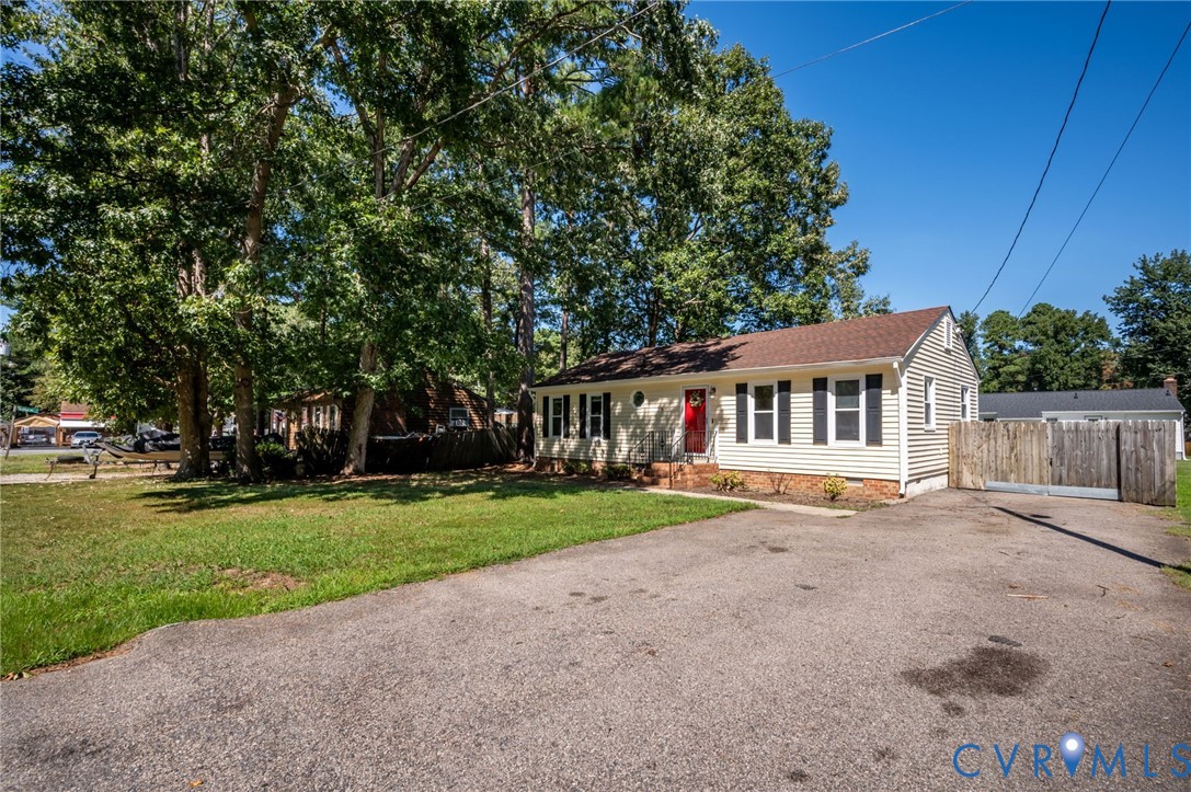 Light-colored siding exterior, red entry door, brown shingle roof, black window shutters, and a gravel driveway