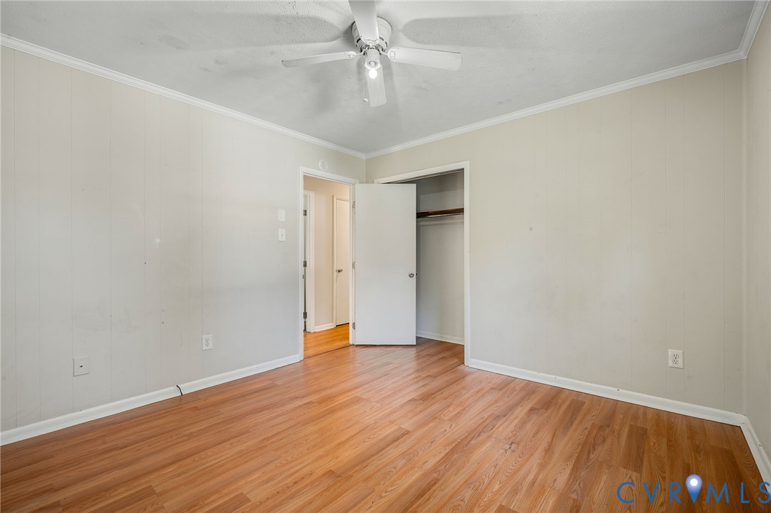 Wood-finish flooring, ceiling fan with integrated lighting, crown molding, and a built-in closet with hanging rod
