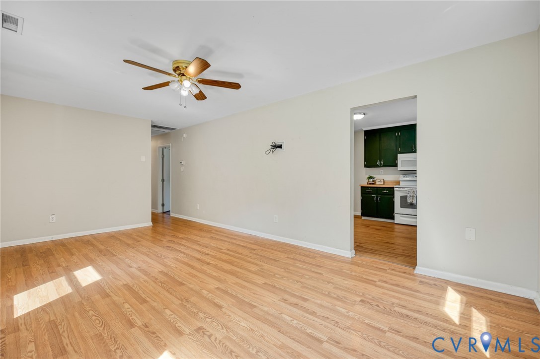Hardwood-style flooring throughout, ceiling fan with light fixture, and a doorway leading to the kitchen featuring dark cabinetry and white appliances