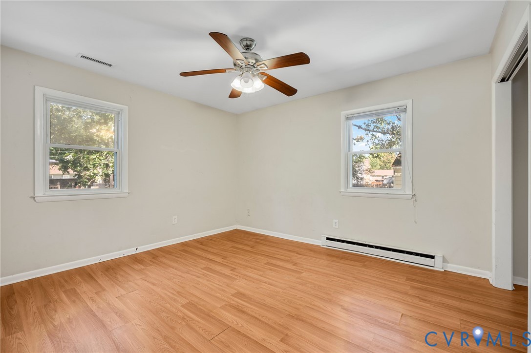Wood-finish flooring, two windows, ceiling fan with light fixture, and light-colored wall paint