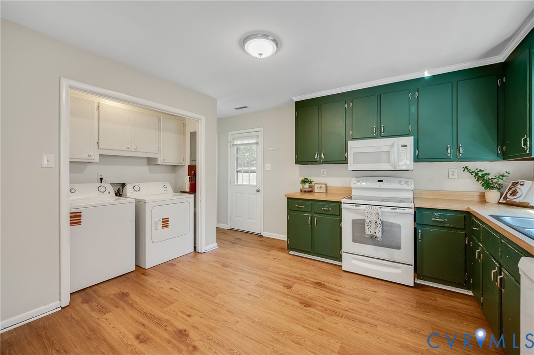 Wood-finish flooring, white appliances, green cabinetry, wood countertops, and a built-in laundry area