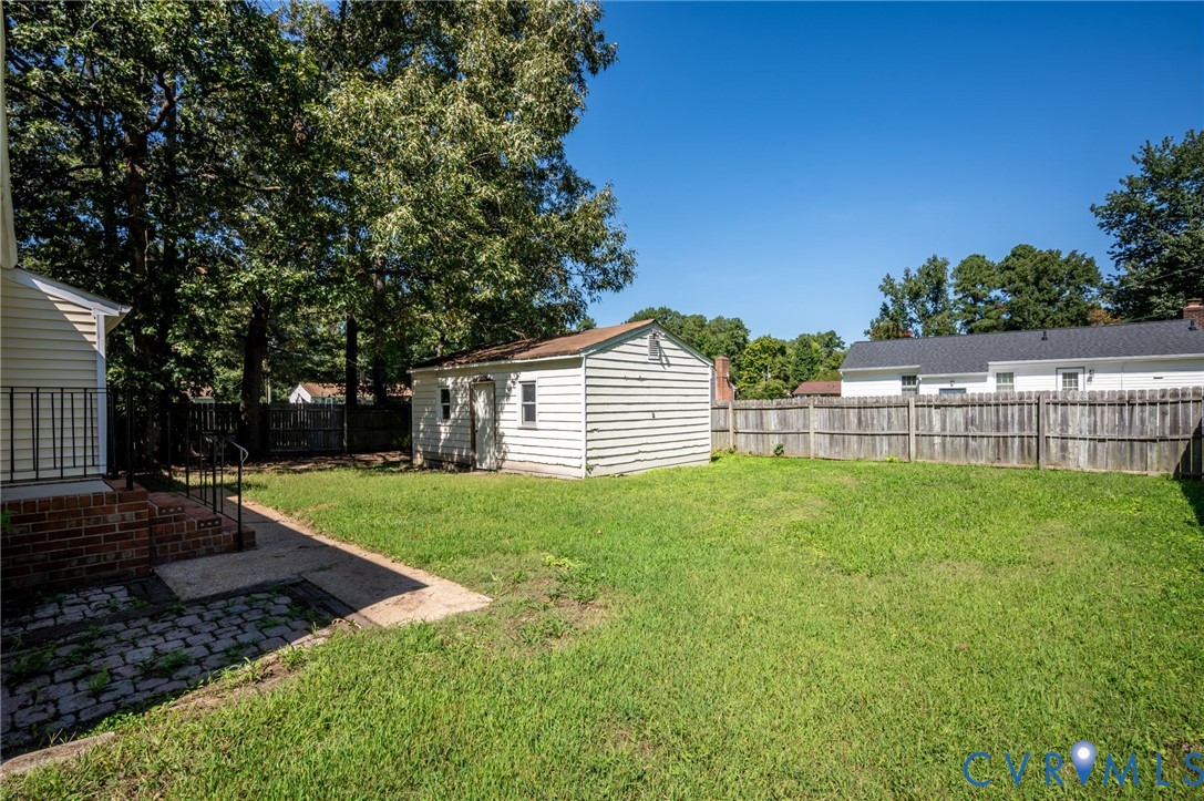 Expansive backyard featuring a lush lawn, mature trees, a detached storage shed, and a privacy fence