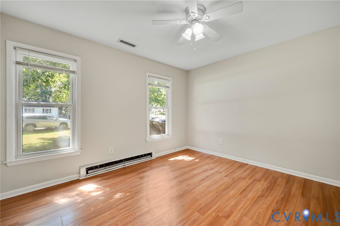 Wood-finish flooring, two large windows, white ceiling fan with integrated lighting, neutral wall paint