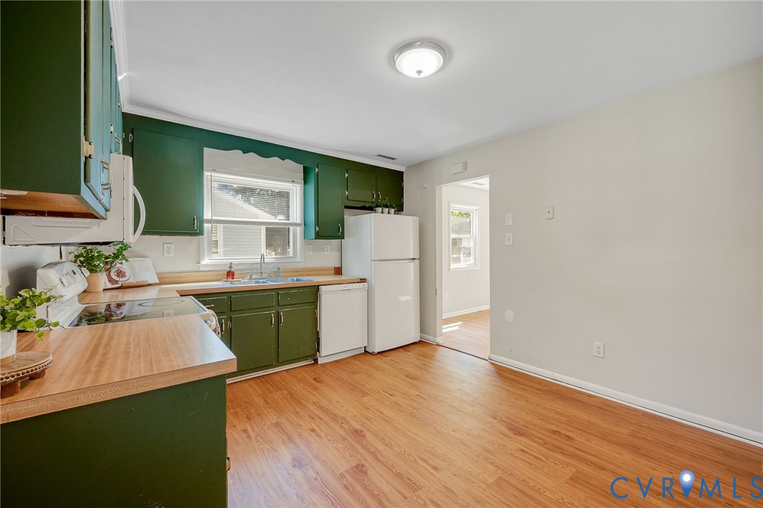 Kitchen with wood-finish flooring, green cabinetry, white appliances, and a window above the sink
