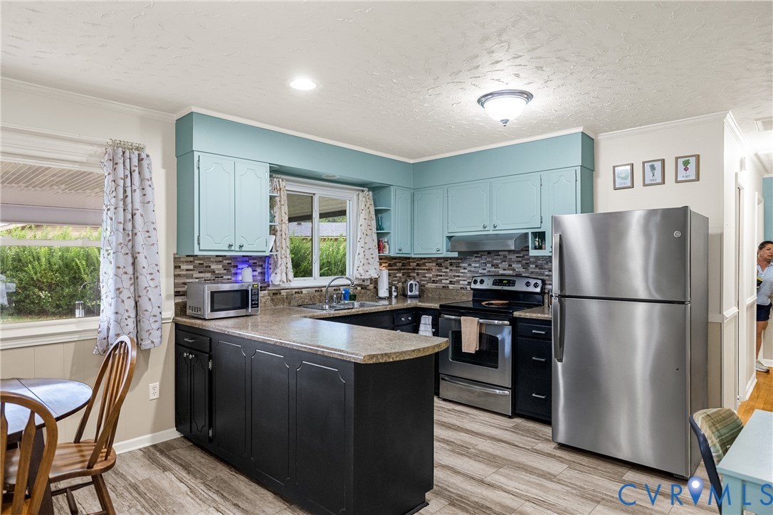 Kitchen featuring wood-finish flooring, light-colored countertops, teal upper cabinetry, dark lower cabinetry, and a mosaic tile backsplash