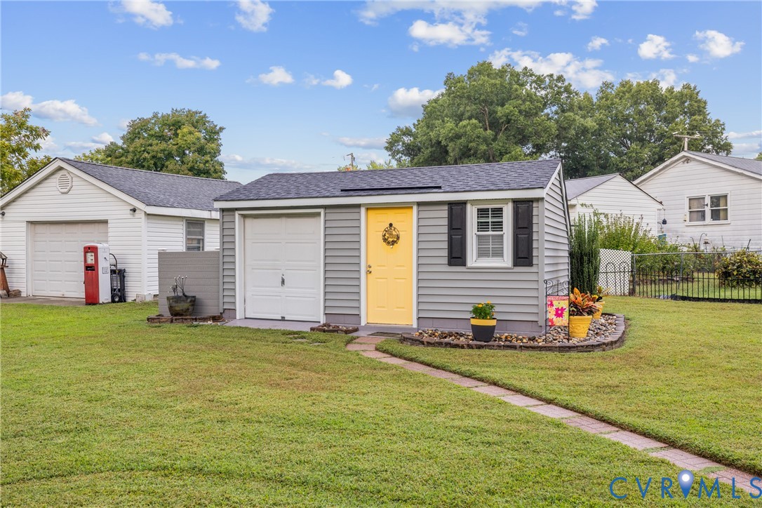 Detached structure featuring a single garage door, a vibrant yellow entry door, exterior siding, and a window with dark shutters