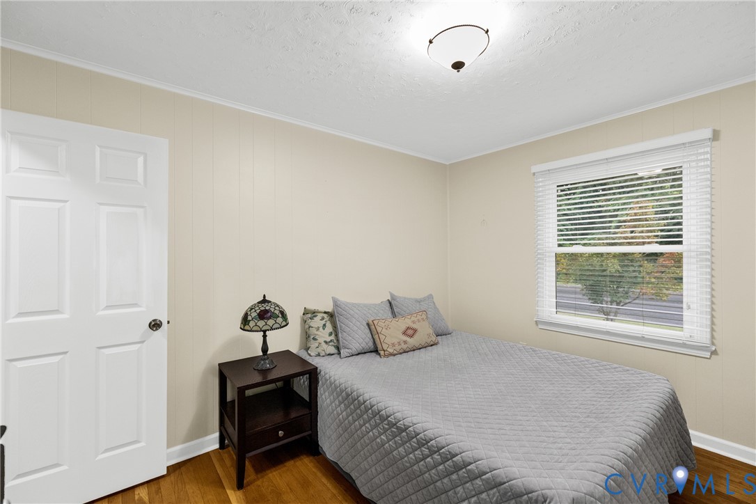Wood-finish flooring, paneled interior door, window with blinds, and ceiling-mounted light fixture