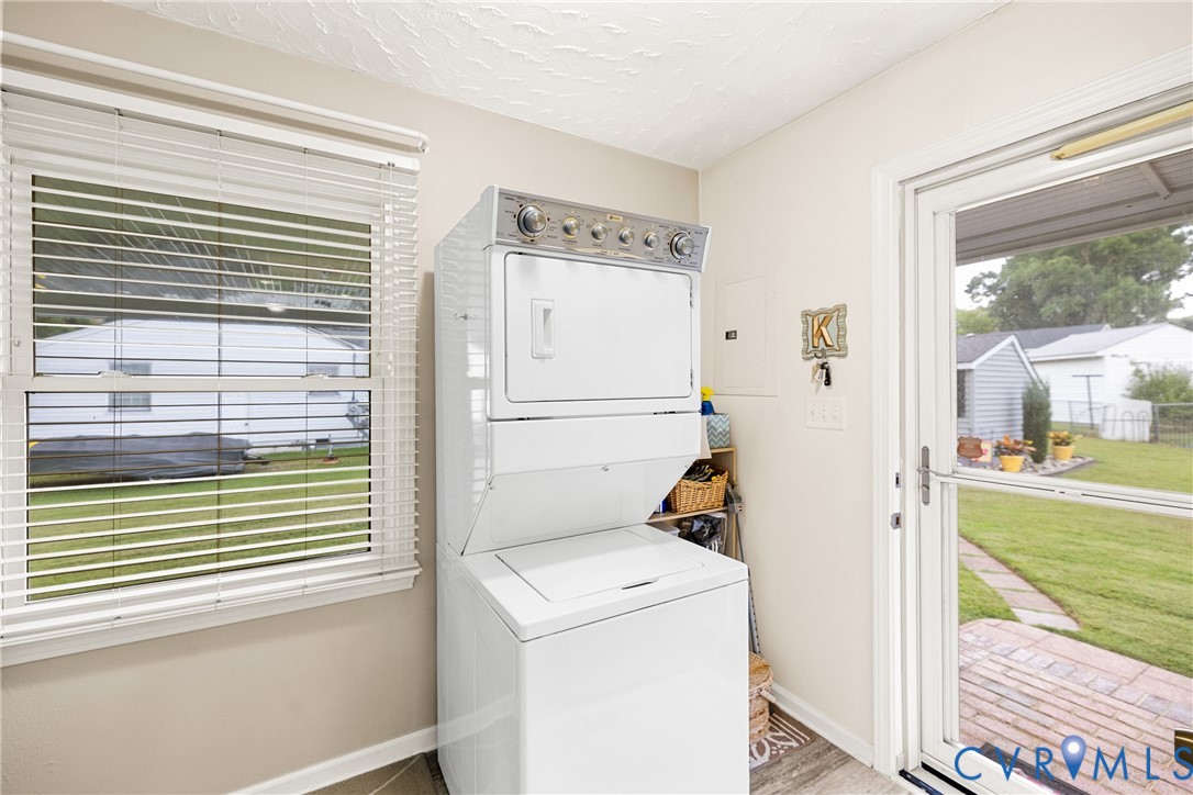Laundry area featuring a stackable washer and dryer, a window with blinds, and a glass-paneled exterior door