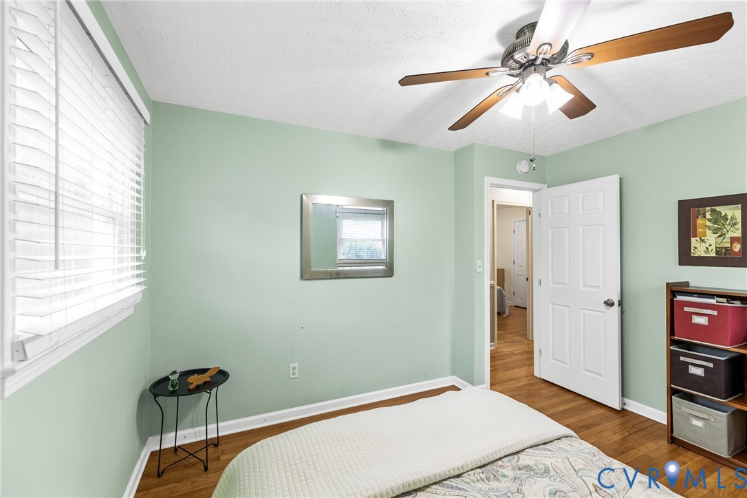 Wood-finish flooring, ceiling fan with integrated lighting, window with blinds, and paneled interior door