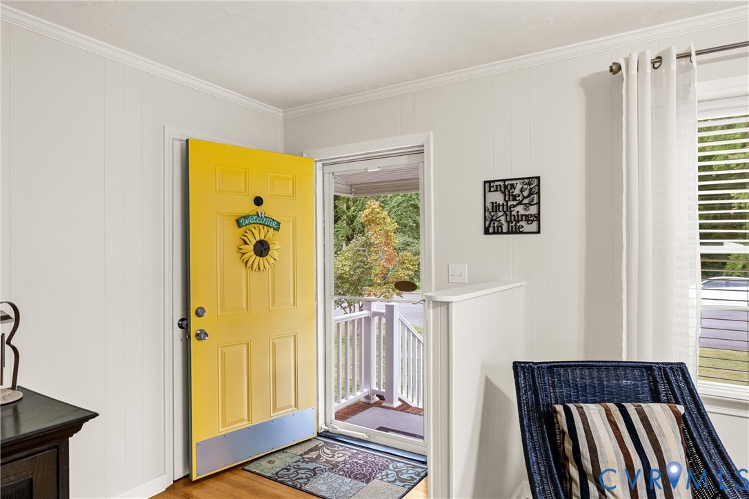 Yellow paneled entry door with white trim, wood-finish flooring, and white wall paneling