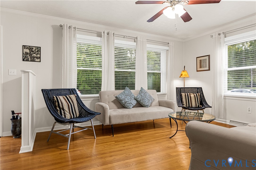 Hardwood flooring, multiple windows with blinds, ceiling fan with light fixture, white wall paneling, and crown molding