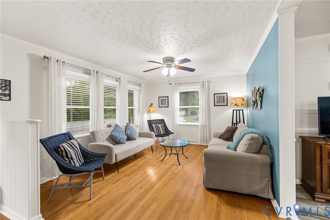 Hardwood flooring, multiple windows with blinds, ceiling fan, crown molding, and wainscoting