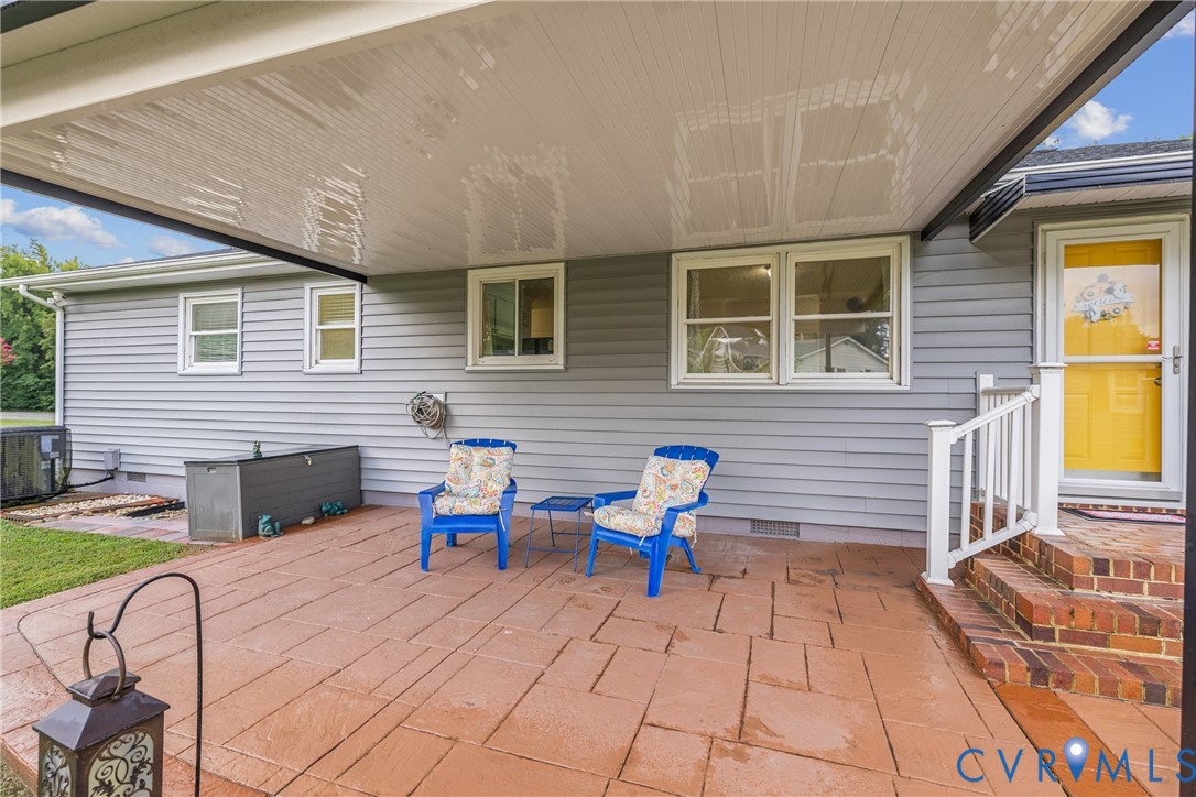 Expansive covered patio featuring stamped concrete flooring, brick steps, and a white railing