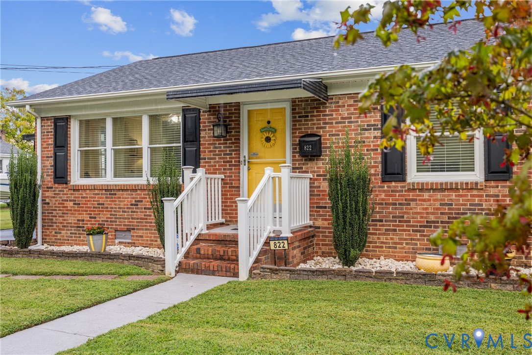 Brick exterior with white trim, dark gray shingles, yellow front door, and white porch railing