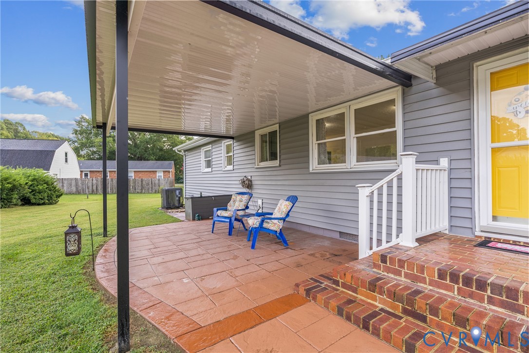 Covered patio featuring stamped concrete, brick steps, and a white railing