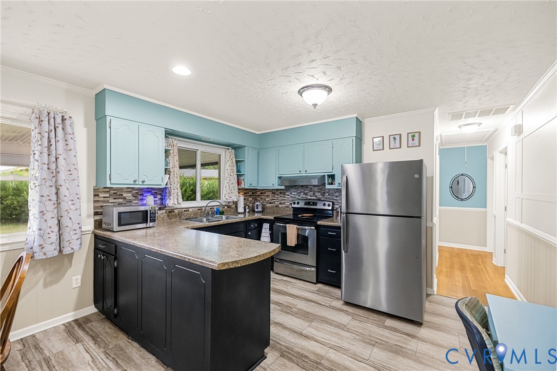 Kitchen featuring wood-finish flooring, two-tone cabinetry, stainless steel appliances, a mosaic tile backsplash, and a breakfast bar