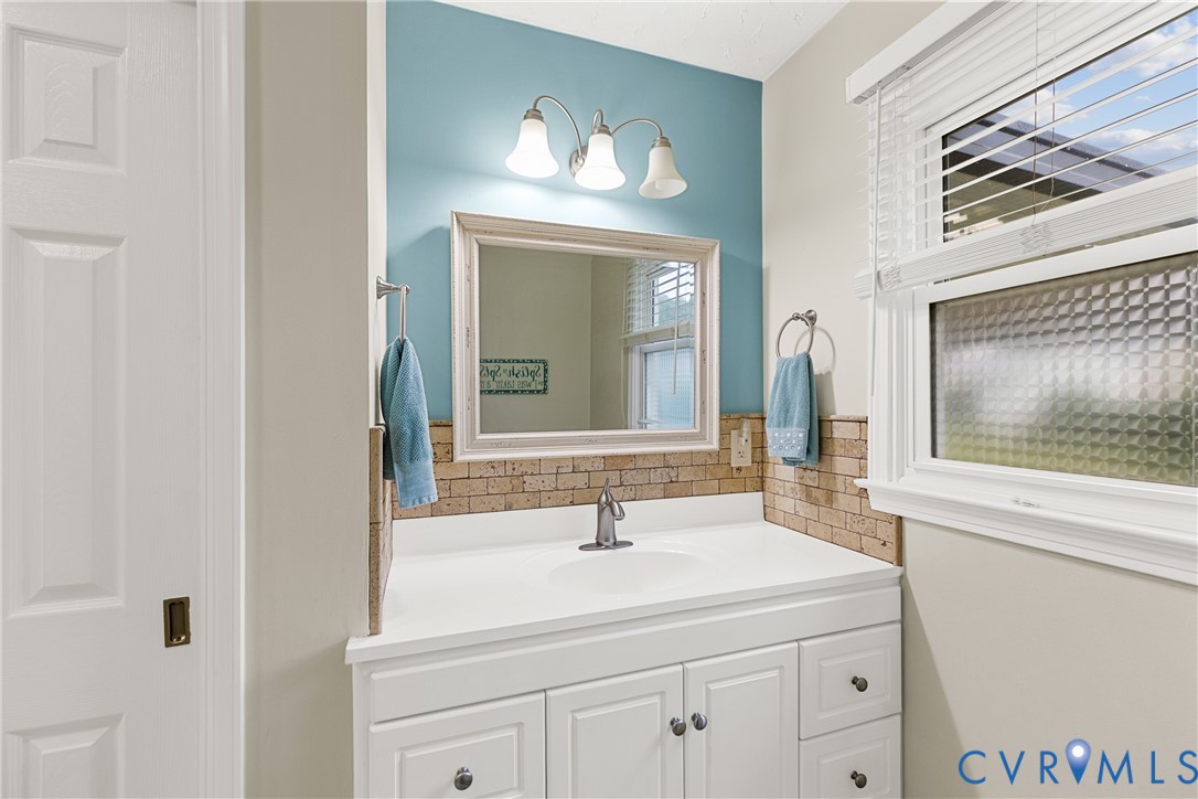 White vanity with an integrated sink and brushed nickel faucet, framed mirror, and a three-light vanity fixture