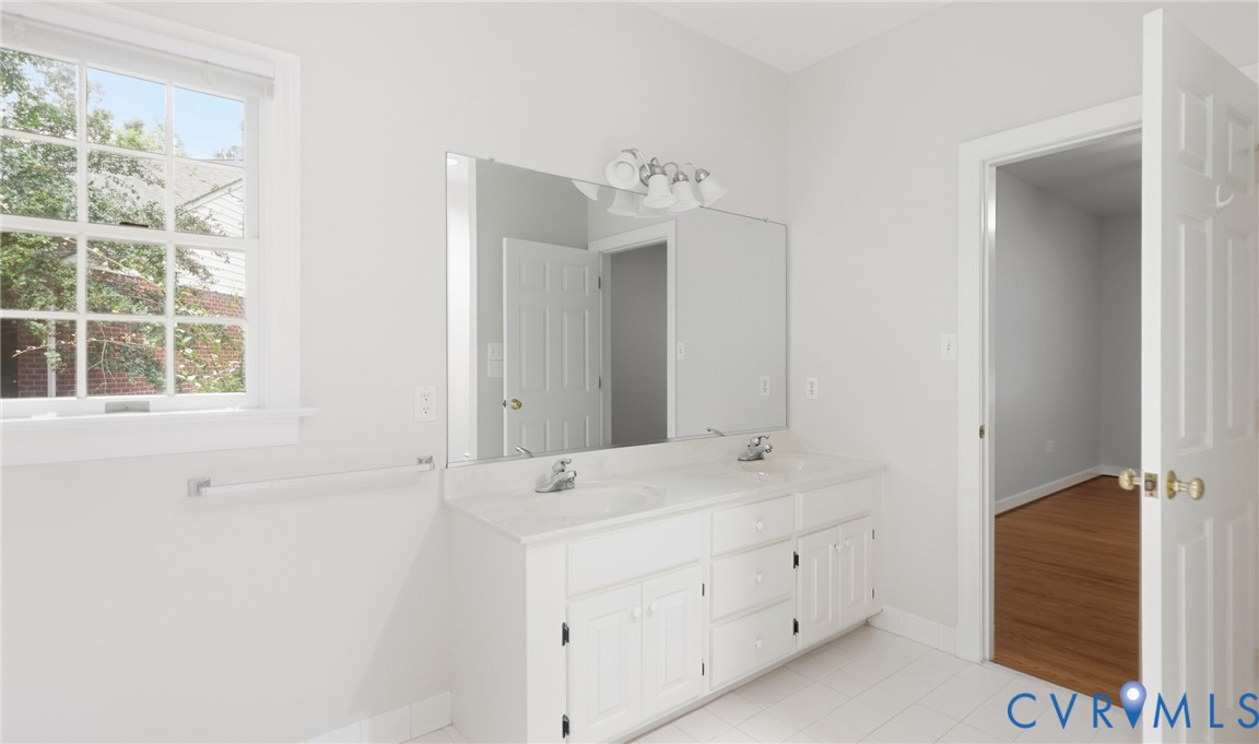 Dual vanity with white cabinetry and integrated sinks, complemented by a large wall-mounted mirror and overhead sconce lighting