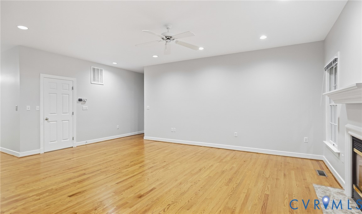 Hardwood flooring, recessed lighting, ceiling fan, white paneled door, and a fireplace with a mantel