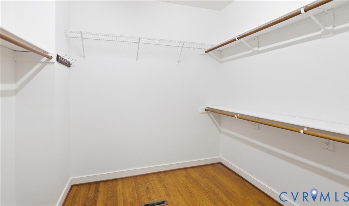 Walk-in closet with wood-finish flooring, wire shelving, and built-in hanging rods
