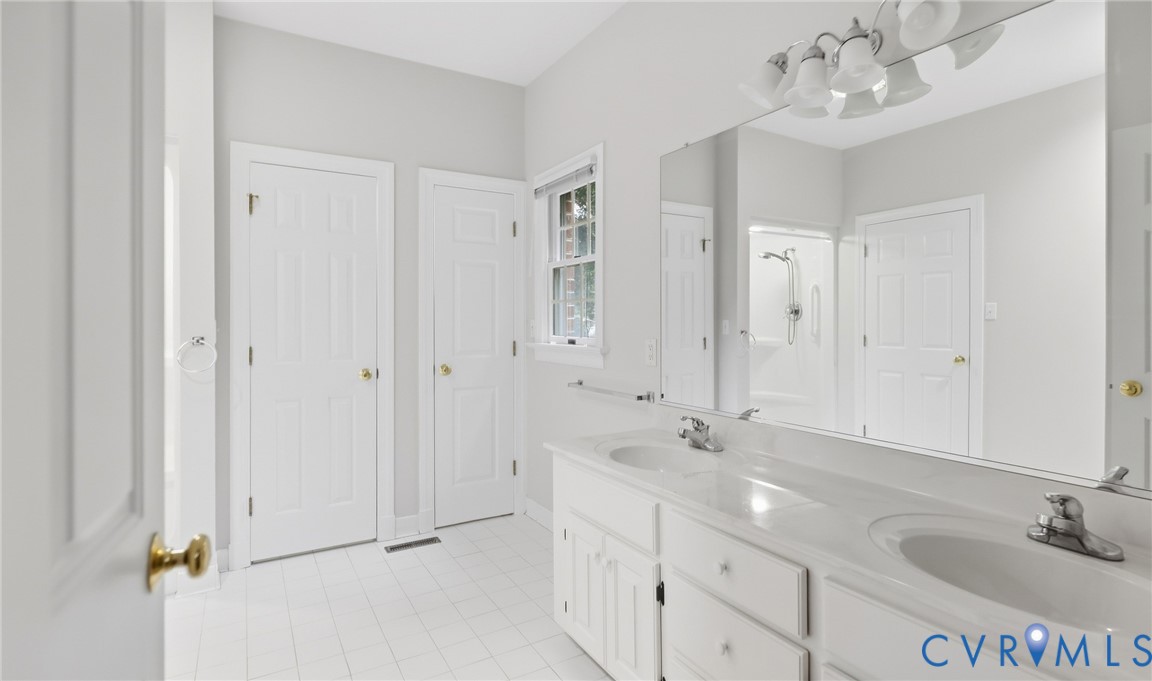 Double vanity with integrated sinks, full-width mirror, white tile flooring, and white paneled doors