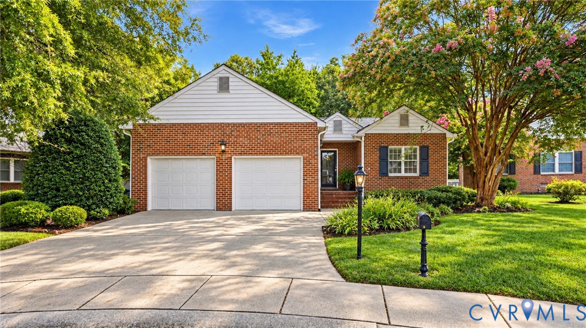 Brick exterior with white siding accents, two-car garage, concrete driveway, front entrance with an exterior light fixture, and a manicured lawn with mature trees Brick exterior with white siding accents, two-car garage, concrete driveway, front entrance with an exterior light fixture, and a manicured lawn with mature trees