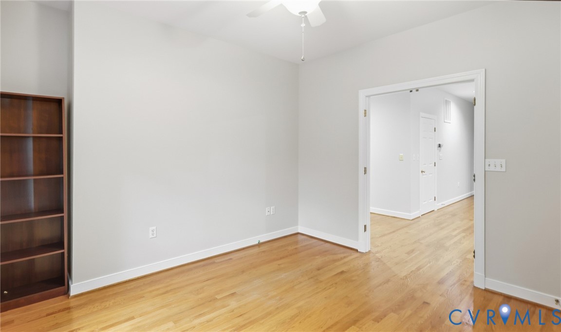 Hardwood flooring, light gray wall finishes, white trim, built-in shelving, and a ceiling fan