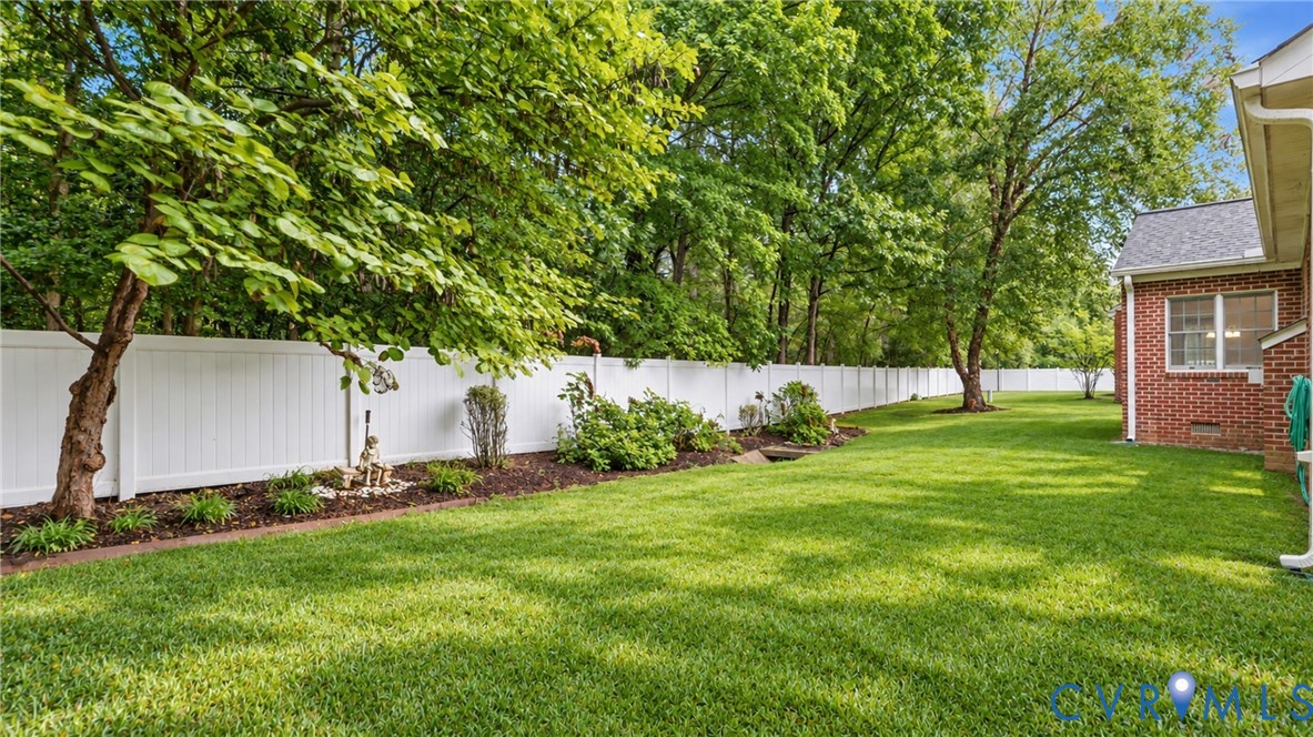 Expansive green lawn, white privacy fence, mature trees, landscaped garden beds, and a brick exterior Expansive green lawn, white privacy fence, mature trees, landscaped garden beds, and a brick exterior