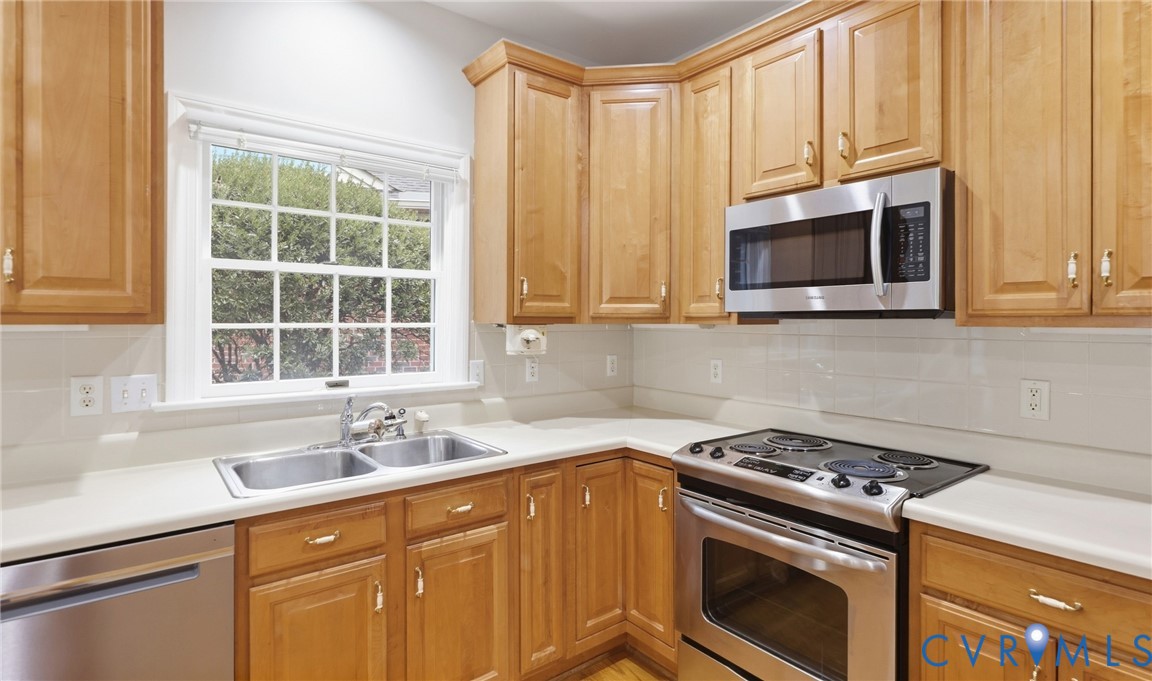 Kitchen featuring wood-finish cabinetry, stainless steel appliances, a double basin sink, and a tiled backsplash