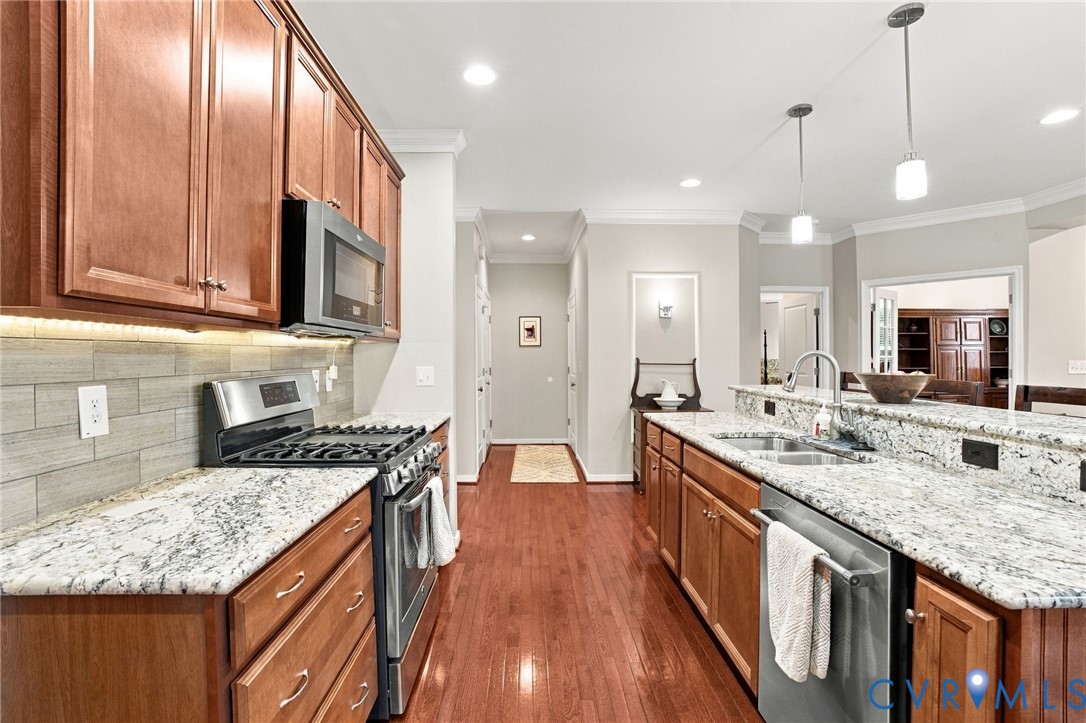 Wood-finish cabinetry, stainless steel appliances, granite countertops, tile backsplash, and wood-finish flooring