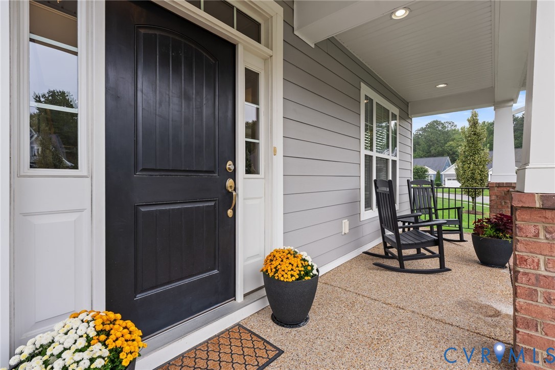 Inviting covered front porch with a dark paneled entry door, sidelight windows, and decorative brick columns